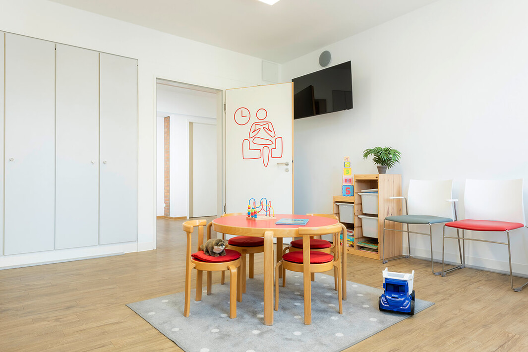 Heller Gruppenraum mit kleinem Tisch, Stühlen und Spielzeug für Kinder.